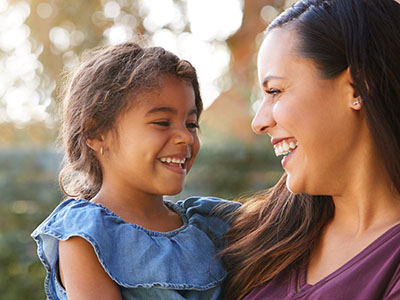 A woman and a young child are smiling at the camera, with the woman holding the child.